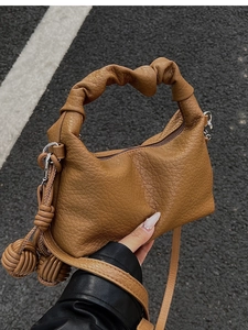 Détail d'un sac plissé marron avec poignée nouée et breloques boules tressées