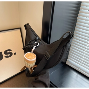 Detail of black nylon crescent bag with adjustable strap and plush coffee cup charm