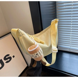 Close-up of pale yellow nylon crossbody bag with adjustable strap and plush coffee charm