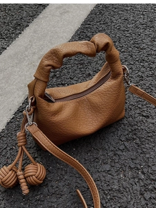 Détail du sac à main marron avec poignée plissée, texture litchi et pendentif boule tressée