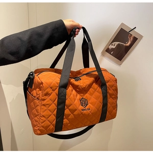 Detail der orangefarbenen Stepp-Reisetasche mit schwarzen Griffen und Markenlogo