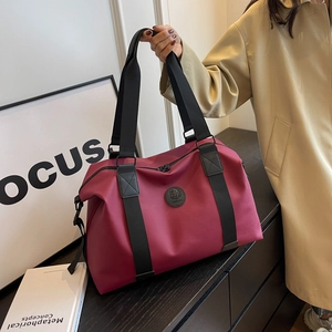 Large capacity burgundy waterproof oxford travel bag with sturdy handles on a wooden table