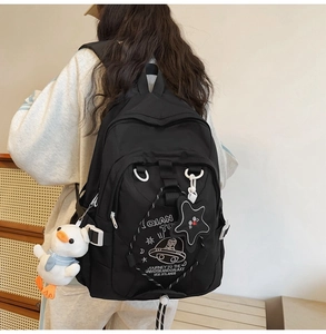 Dettaglio dello zaino nero in nylon con stampe spaziali e ciondoli in peluche carini