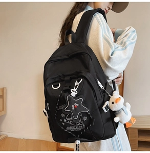 Dettaglio dello zaino nero in nylon con ciondolo a stella e accessorio papera di peluche