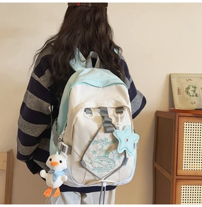 Zaino in tela blu e beige da donna indossato con ciondoli a forma di papera e stella
