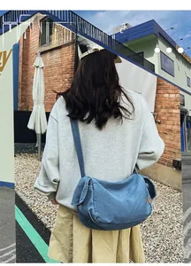 Outdoor shot of large blue denim crossbody bag shown on model with vintage brick background