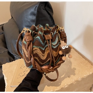 Detalle del bolso tipo cubo de punto con diseño de ondas, asa de cuero y colgante de peluche