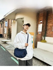 Navy blue denim crossbody bag shown on a model against a modern red brick wall