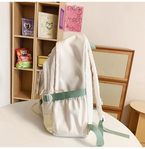 Dettaglio dello zaino in nylon crema con spalline verdi e tasche laterali su tavolo