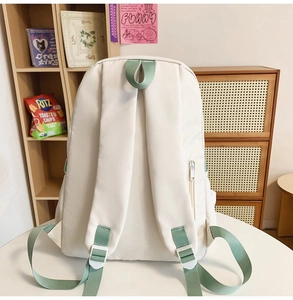 Dettaglio dello zaino beige con spallacci verdi e tasca posteriore con cerniera