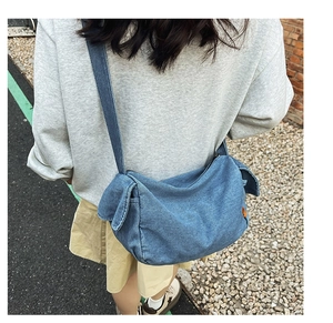 Detailed view of a blue denim crossbody bag featuring a unique side knot and curved shape