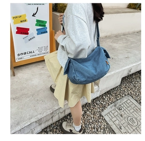 Detail of blue denim crossbody bag with adjustable strap and leather accent on urban stairs