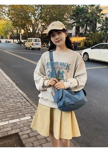 Blue denim crossbody bag styled with a casual sweatshirt and pleated skirt outdoors