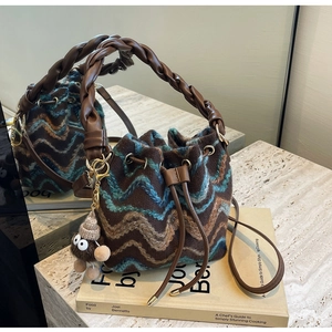 Detalle de un bolso tipo cubo de punto marrón con patrones de ondas y asa trenzada gruesa