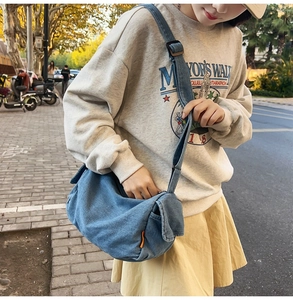 Detailed side view of denim crossbody bag with adjustable strap and orange label