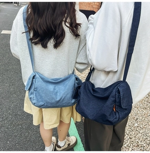 Detail of light and dark blue denim crossbody bags worn by models in outdoor city street