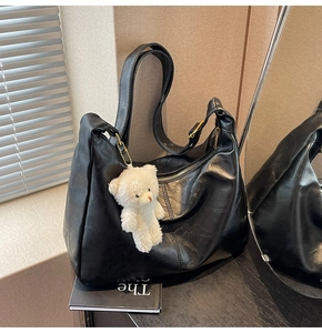 Detail of black faux leather crescent tote bag with cute plush bear charm and gold zipper