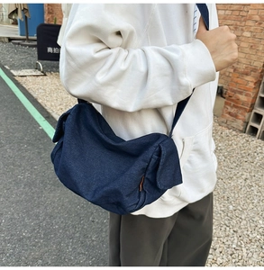 Detail of dark blue denim crossbody bag featuring orange side label and soft texture