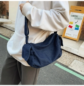 Detail of dark blue denim crossbody bag with side flap pocket and adjustable strap