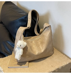Close-up of beige tote bag with smooth leather texture, zipper closure and plush bear charm