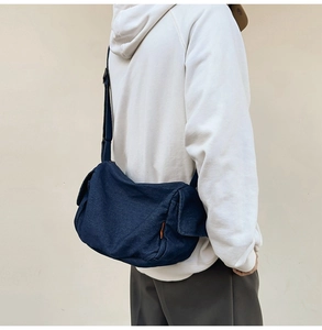 Detail view of the deep blue denim messenger bag showing the fabric texture and orange tag