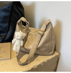 Detail view of beige PU leather hobo bag on a stone stand with a plush bear charm
