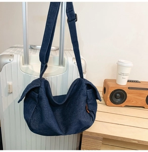 Detail of dark blue denim crossbody bag hanging on white luggage for travel scene