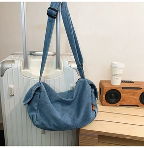 Detail view of denim crossbody bag with orange side label and adjustable shoulder strap