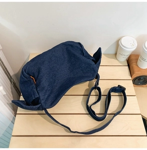 Detail of soft dark blue denim crossbody bag with adjustable strap on wooden table