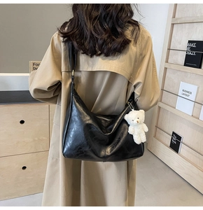 Detail of glossy black hobo tote bag with plush bear charm on a warm trench coat