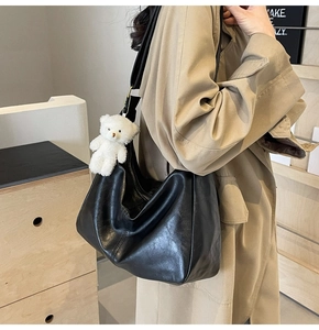 Close-up of black leather hobo tote with litchi texture and cute white teddy bear charm