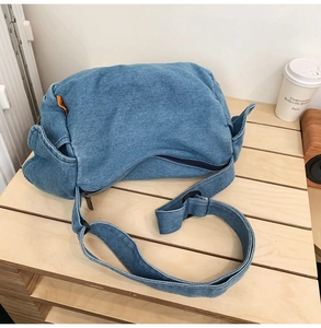 Detail of blue denim crossbody bag with orange woven label on a wooden stand