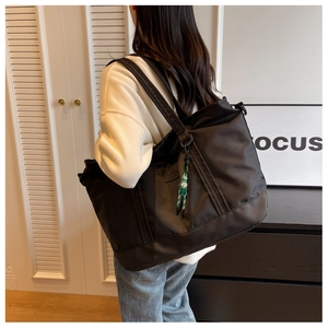Detailed view of large black travel tote with wide strap and green woven pendant