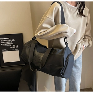 Detail of a large black nylon travel bag featuring embossed letters and a wide crossbody strap