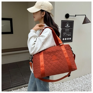 Detail of quilted orange travel bag featuring embroidered logo and wide nylon handle