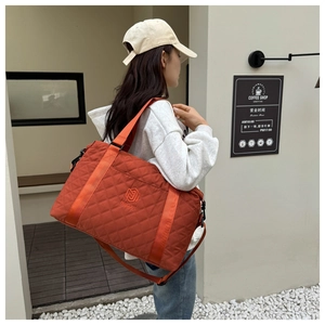 Detailed outdoor shot of brick red quilted travel bag with logo embroidery and shoulder strap