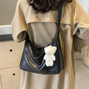 Classic black PU hobo tote bag with plush bear charm worn by a model in warm light