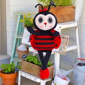 Macro detail of plush ladybug toy with red bow and striped body in a garden setting