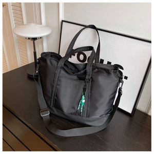 Macro shot of large black nylon travel tote featuring a logo patch and woven tassel charm
