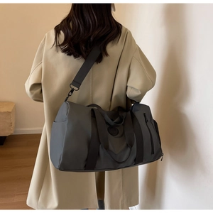 Back view of a model carrying a large dark grey nylon travel bag with shoulder strap