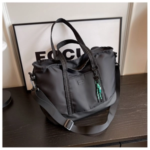 Macro detail of a large black nylon travel tote with adjustable strap and green decorative knot
