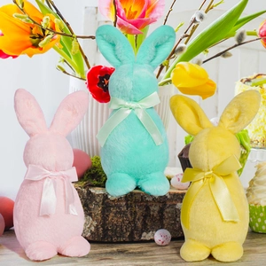 Trois lapins de Pâques en peluche rose, menthe et jaune avec nœuds sur un socle en bois rustique