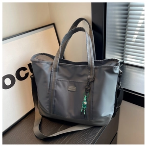 Detail of grey travel bag with NINCUIA logo patch and green doll charm accessory