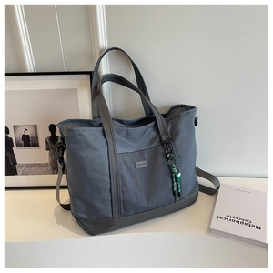 Detail of grey-blue large travel tote with detachable strap and woven charm accessory
