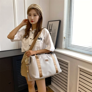 Grand sac de voyage gris en tissu Oxford avec anses dorées, porté par une femme