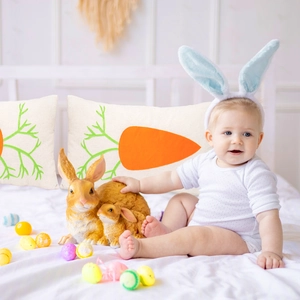 Easter carrot print pillow with rabbit figurines and colorful eggs around a baby