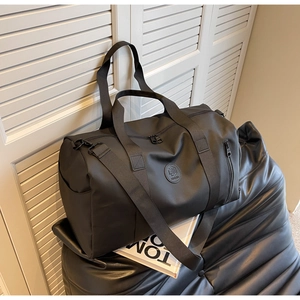 Black nylon travel bag with side zipper pocket and adjustable strap on a leather seat
