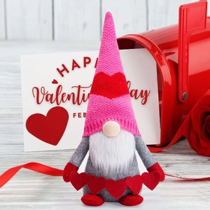 Macro shot of a pink Valentine's gnome with knitted hat and heart bunting on wood