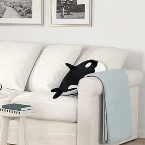 Detail of a plush orca whale pillow resting on a modern white fabric sofa in a cozy room
