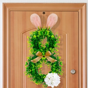 Detalle de corona de Pascua con forma de conejo y hojas verdes sobre puerta de madera